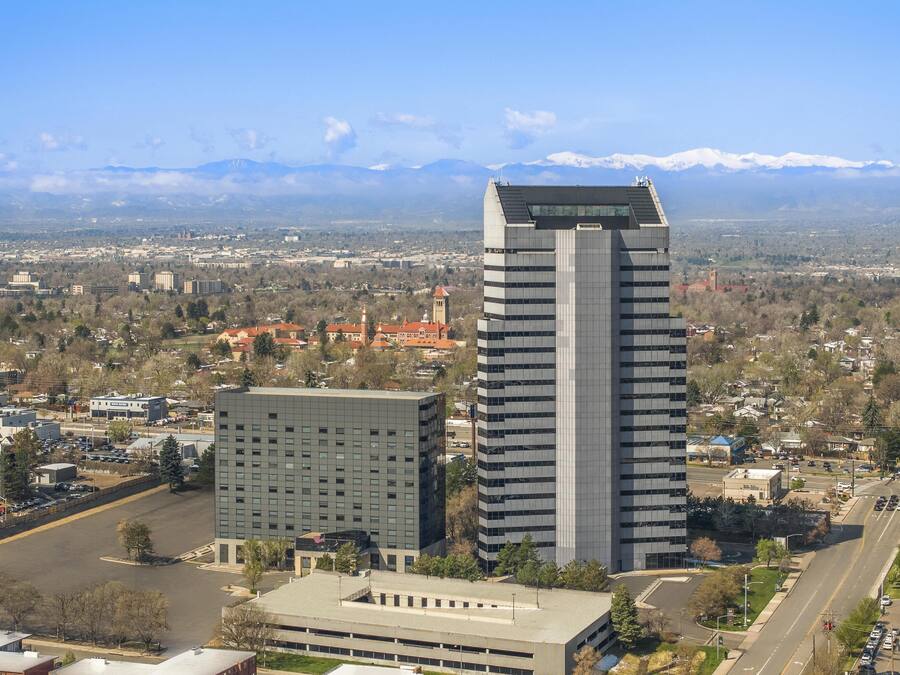 Un edificio de gran altura con diseño moderno, rodeado por un paisaje urbano y montañas al fondo.