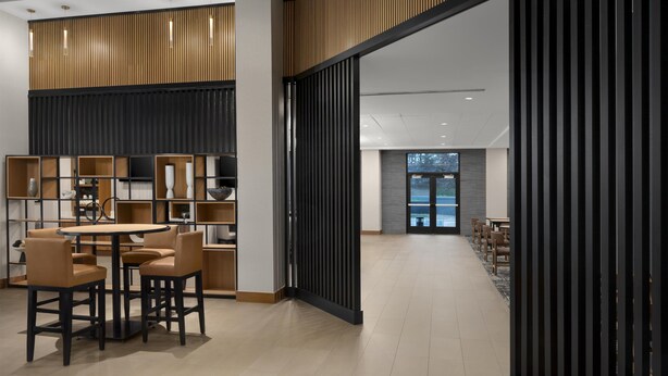 A modern interior with a round table and chairs, wooden paneling, and a view through a glass door. - Hyatt Place Denver/Cherry Creek (Glendale)
