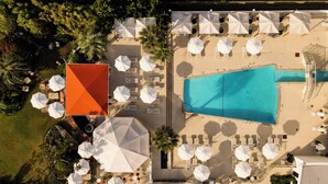 An aerial view of a resort with a swimming pool, multiple lounge areas with umbrellas, and a distinct orange building. - Trailborn Surf and Sound, Outdoor Collection by Marriott Bonvoy (Wrightsville Beach)