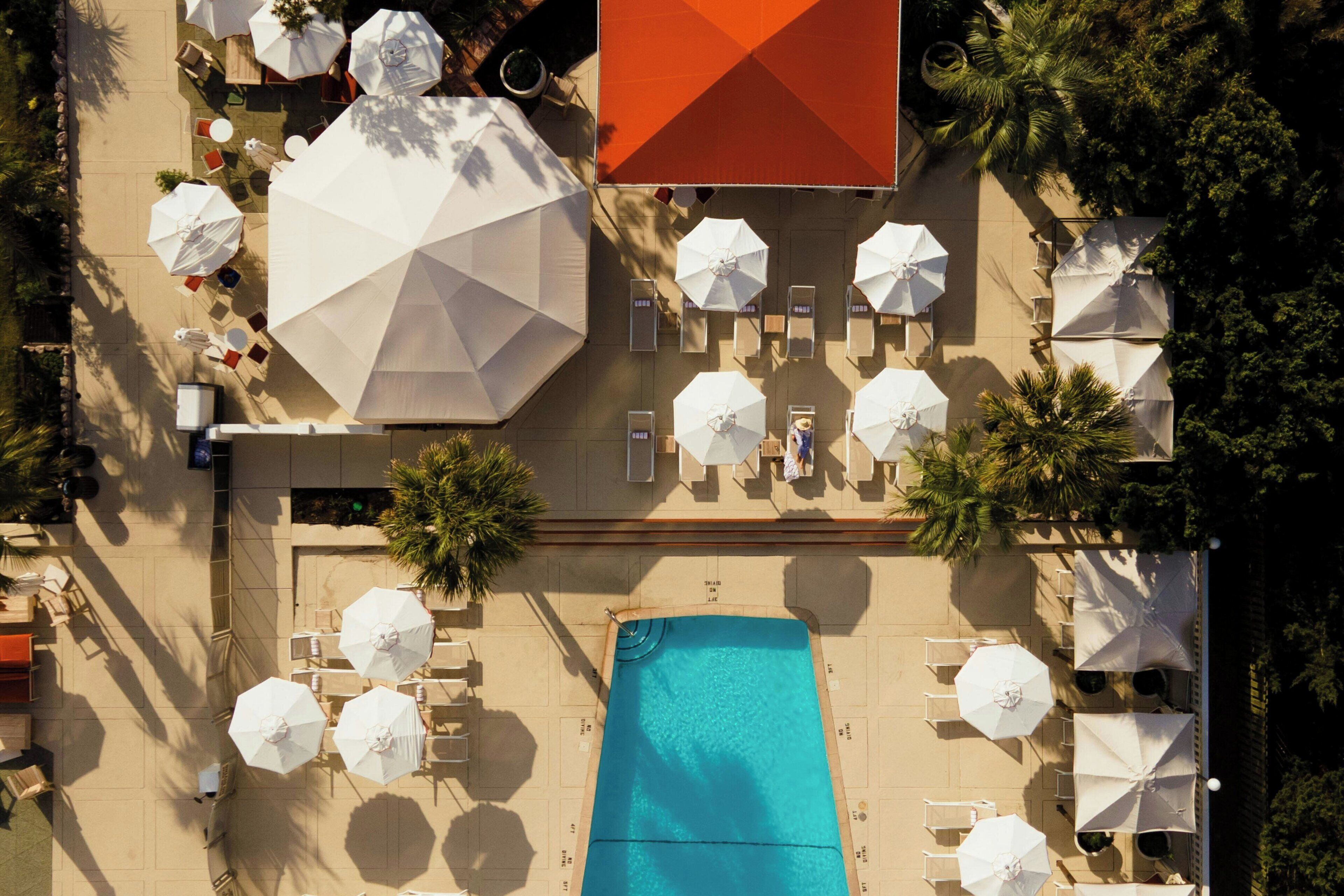 An aerial view of a hotel pool area with multiple white umbrellas, lounge chairs, and a large rectangular pool.