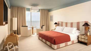 Una habitación de hotel con cama, mesitas de noche, una silla, un escritorio y una ventana con cortinas.