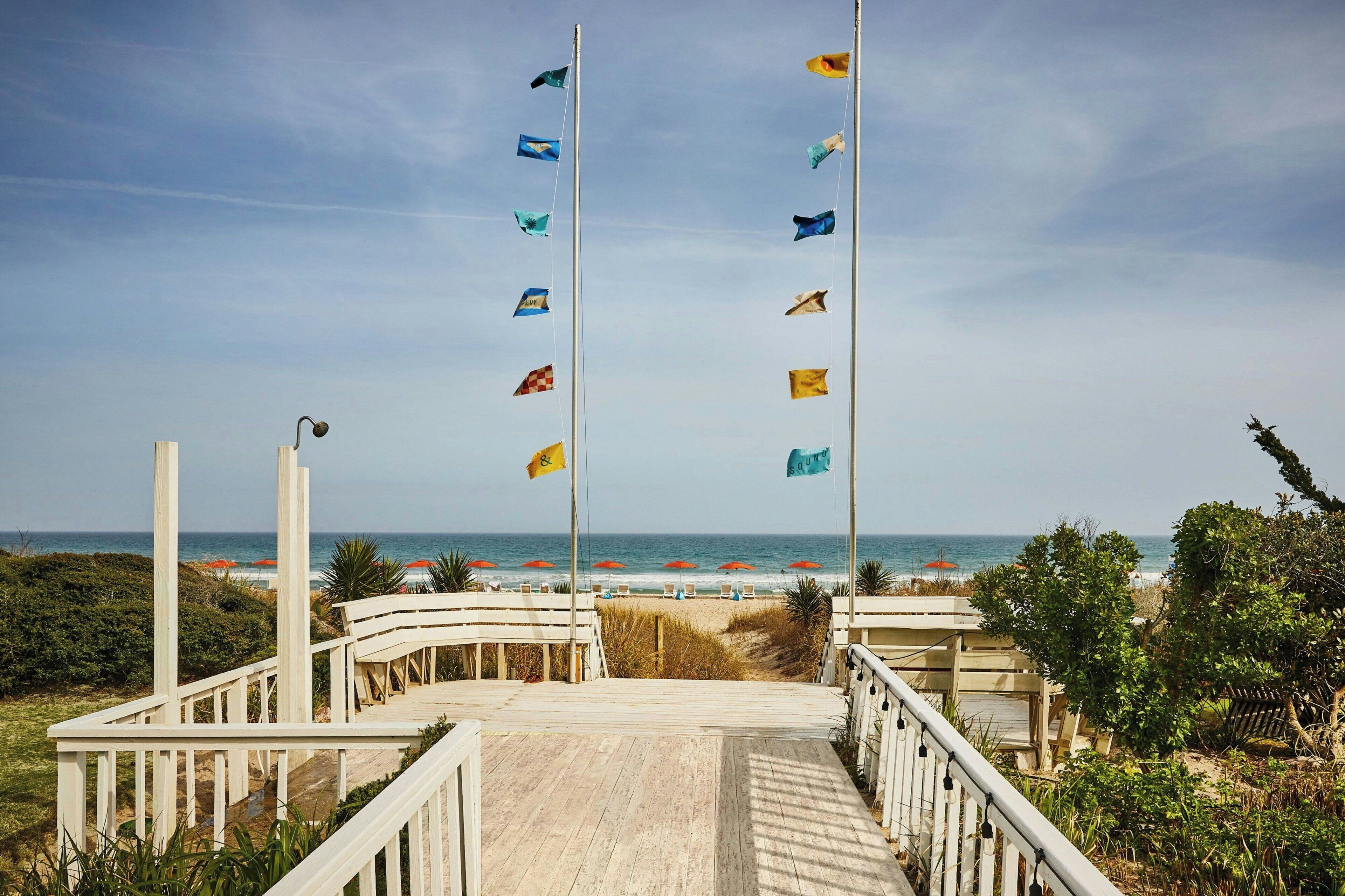 A wooden boardwalk leading to a beach with flags and umbrellas.