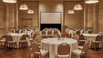 A conference room with multiple round tables, chairs, and large hanging lamps.
