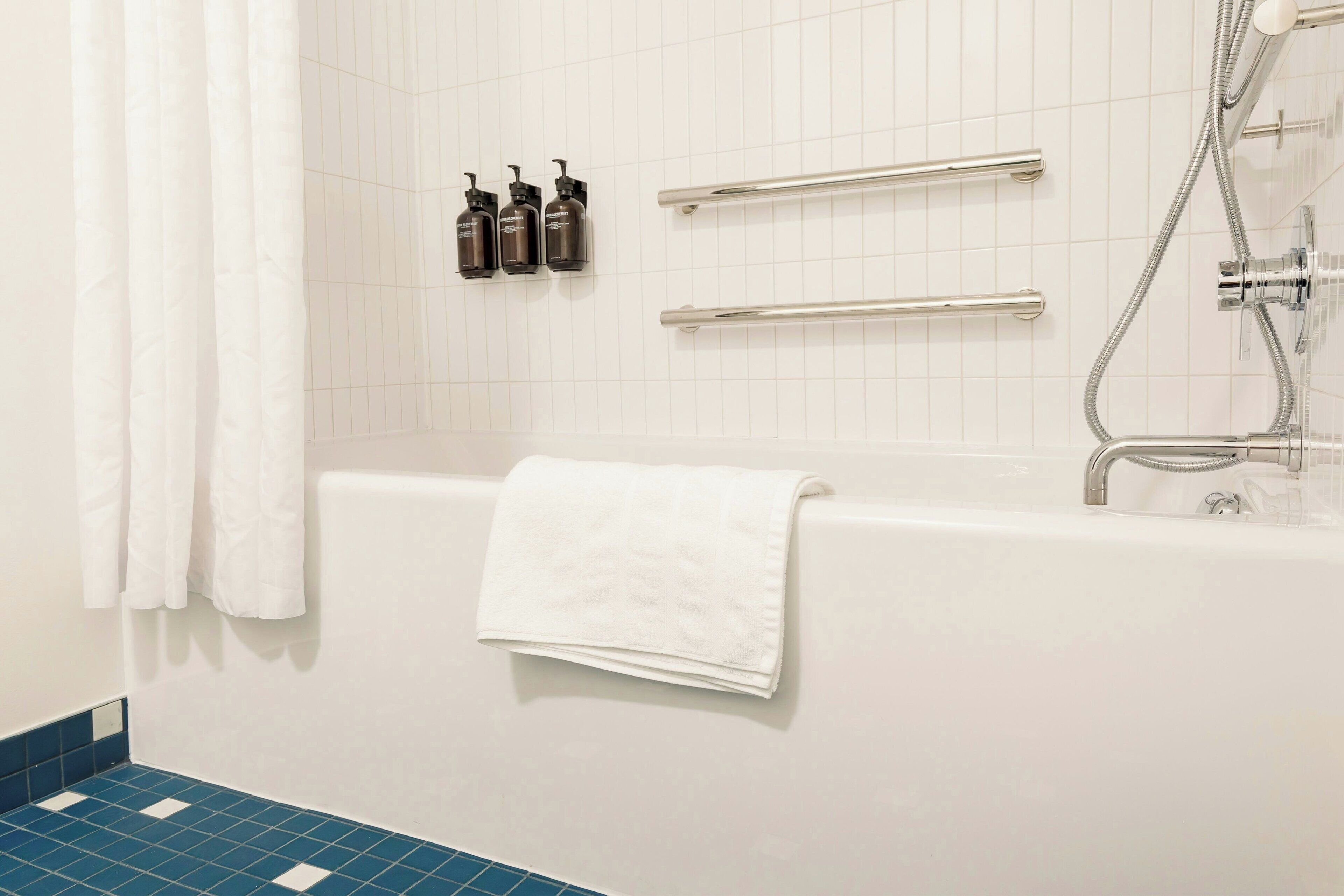 Een badkamer met een witte badkuip, een witte handdoek en drie shampoos op de muur.