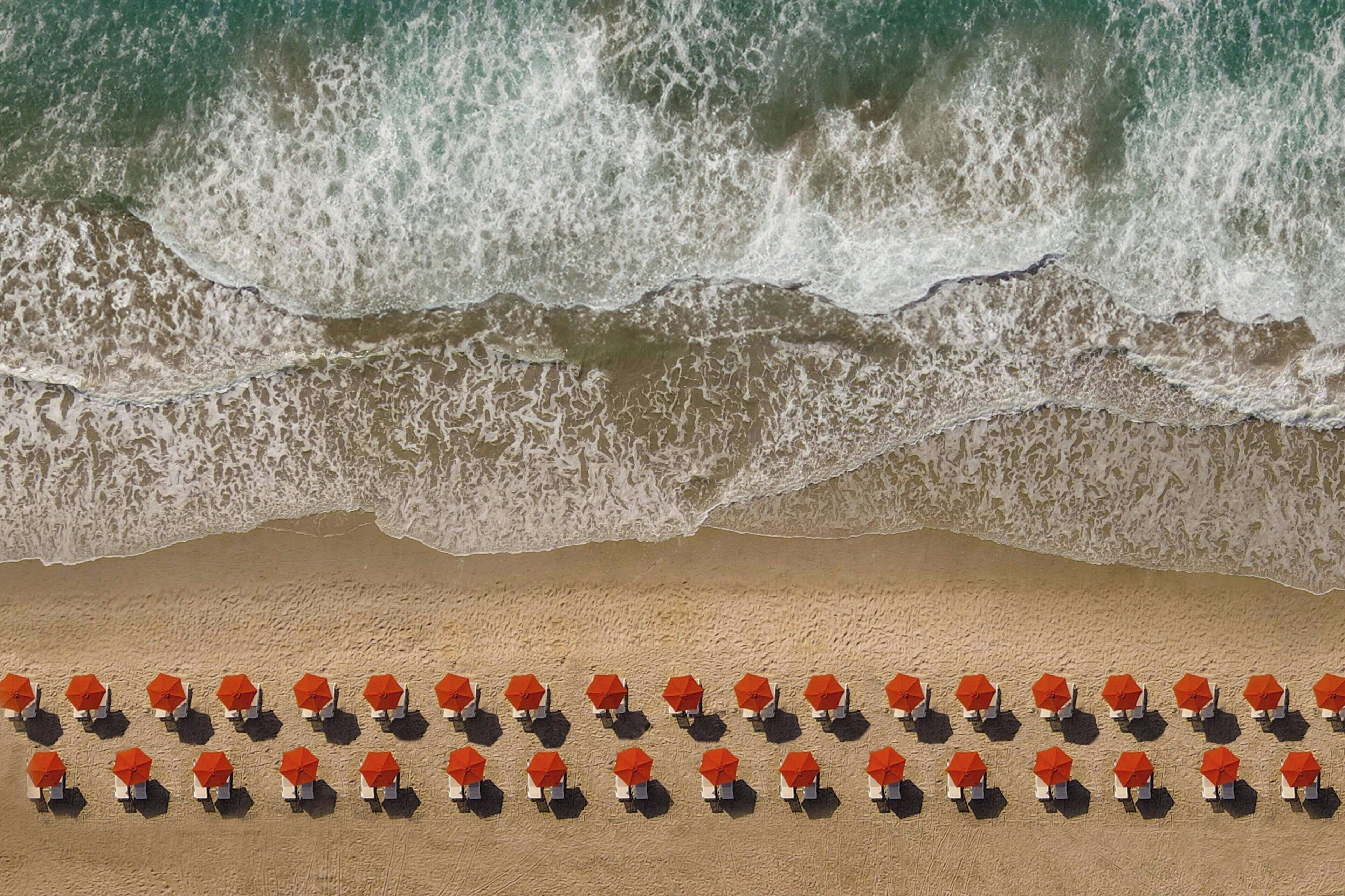 A beach with rows of orange umbrellas and chairs, and waves crashing onto the shore.