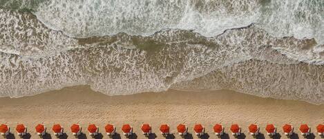 A beach with rows of orange umbrellas and chairs, and waves crashing onto the shore.