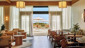 Un hall d’hôtel doté d’un espace salon, offrant une vue sur la terrasse extérieure, et agrémenté d’une grande fenêtre avec des rideaux.