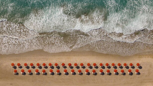 Une plage bordée de rangées de parasols orange et de chaises blanches.