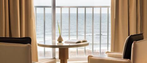Ein Zimmer mit Meerblick, ein runder Tisch mit einem Buch und einer Vase, und zwei Stühle.