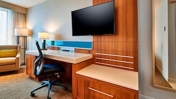 Une chambre d’hôtel avec un bureau en bois, un téléviseur à écran plat fixé au mur, un canapé confortable et une lampe.
