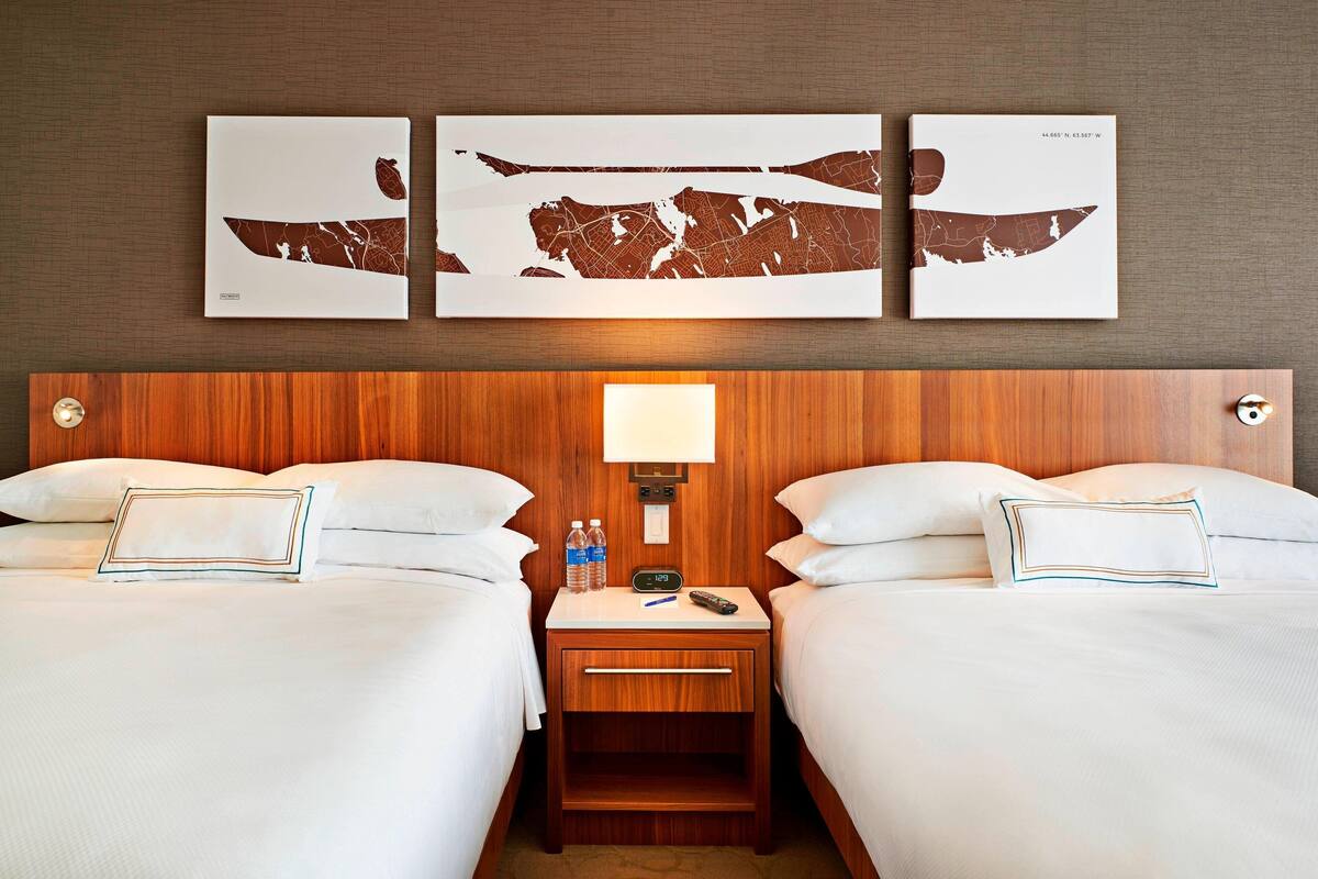 A hotel room with two beds, a nightstand with a lamp, and three wall-mounted artworks.