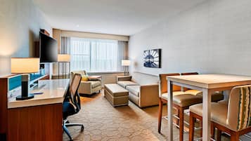A hotel room with a desk, computer, chair, sofa, and dining table with chairs.