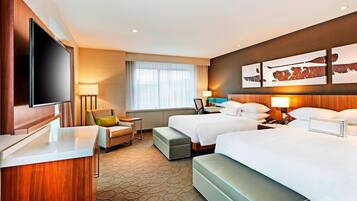 A hotel room with a large flat-screen TV, two beds, a desk, and a chair.