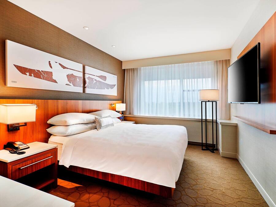 Une chambre d’hôtel avec un grand lit, un téléviseur à écran plat, un bureau avec une lampe et une fenêtre avec des rideaux.