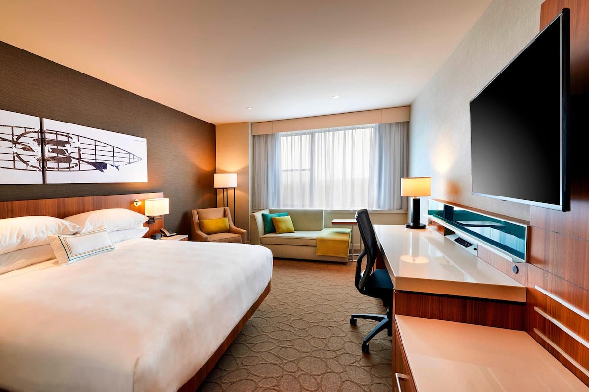 A hotel room with a large bed, a desk, a chair, a sofa, a TV, and a window with curtains.