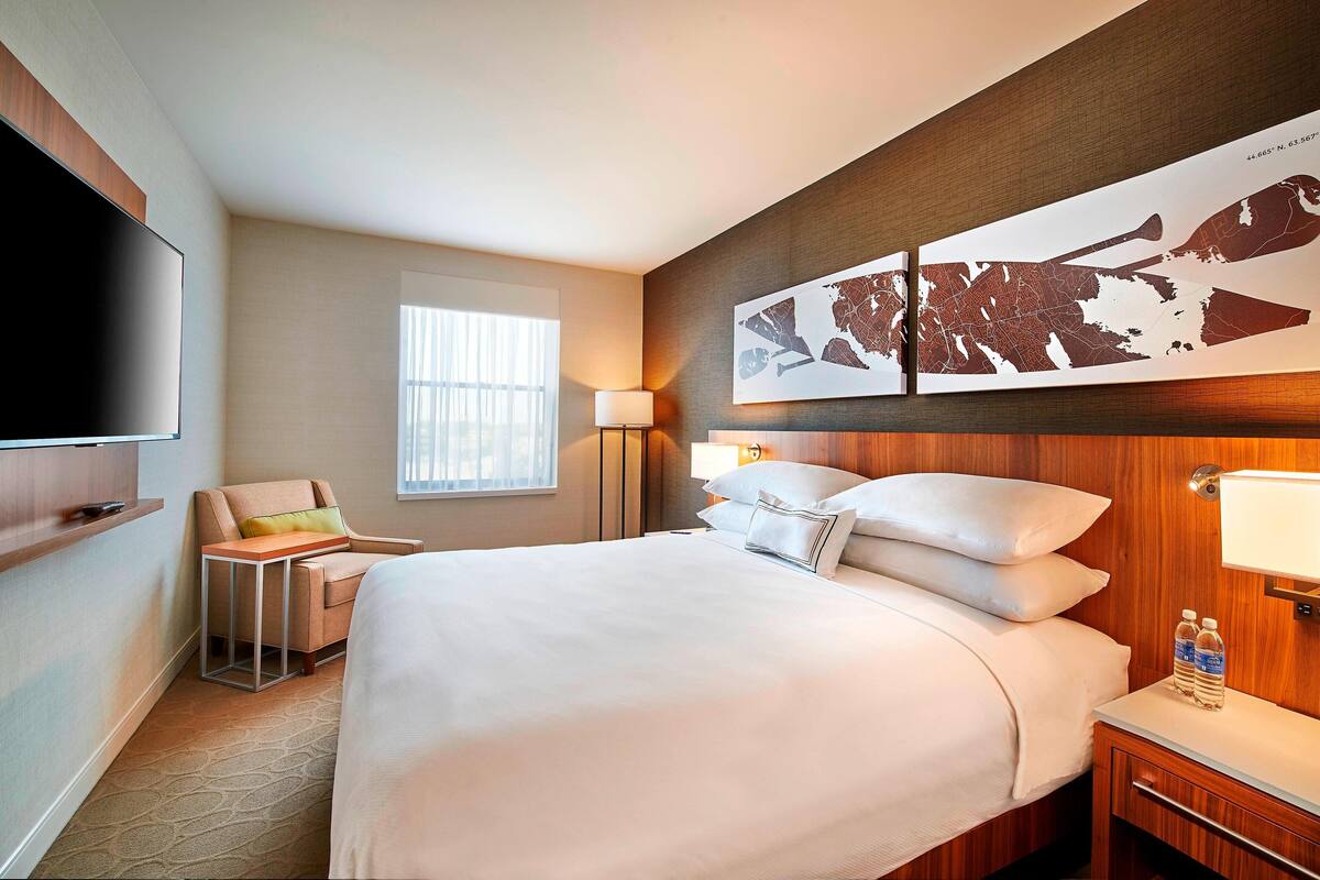 A hotel room with a large bed, a flat-screen TV, a chair, a desk, and a map artwork on the wall.