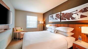 A hotel room with a large bed, a flat-screen TV, a chair, a desk, and a map artwork on the wall.