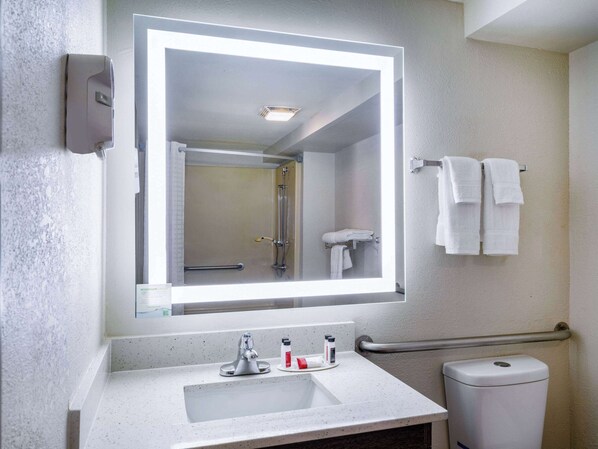 Un baño con un espejo grande, un lavabo, un secamanos y un perchero para toallas.