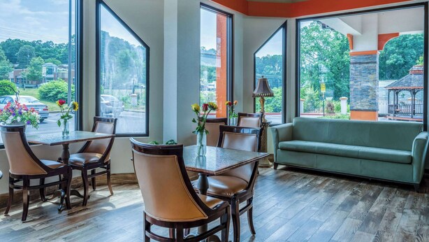 Ein Essbereich mit Tisch und Stühlen, große Fenster mit Ausblick nach draußen und ein grünes Sofa.