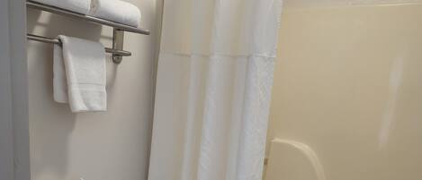 A bathroom with a toilet, a towel rack with towels, a toilet paper holder, and a shower with a curtain.
