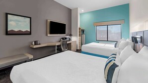 Ein Hotelzimmer mit Bett, Schreibtisch, Stuhl, Fernseher und Fenster mit Blick auf die Stadt.