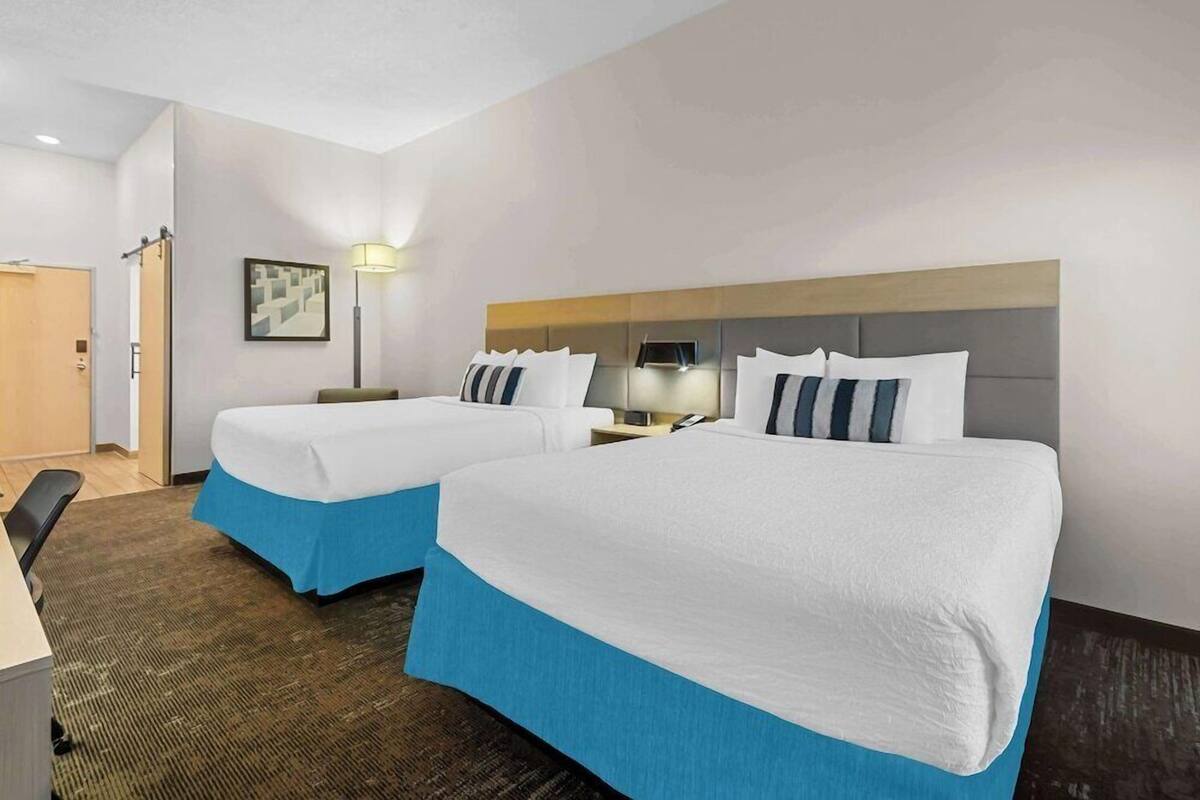 A hotel room with two beds, a desk, a chair, a lamp, and a framed picture on the wall.