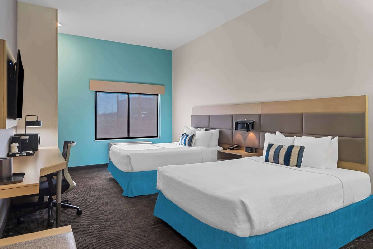 A hotel room with two beds, a desk, a chair, a TV, and a window.