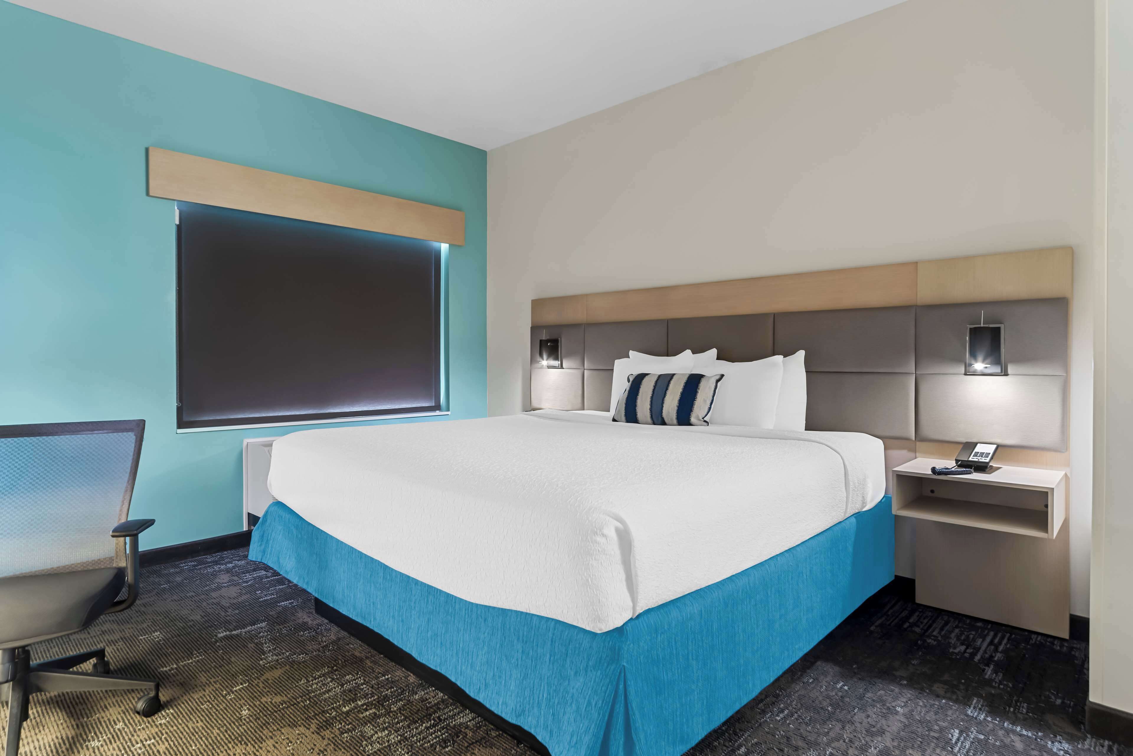 Une chambre d’hôtel avec un grand lit, un bureau, une chaise et une fenêtre avec des stores.