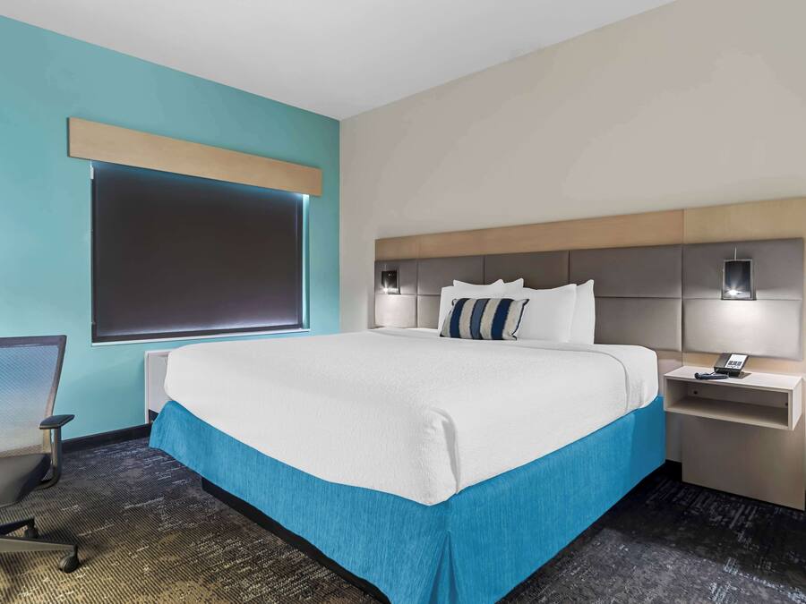 A hotel room with a large bed, a desk, a chair, and a window with blinds.