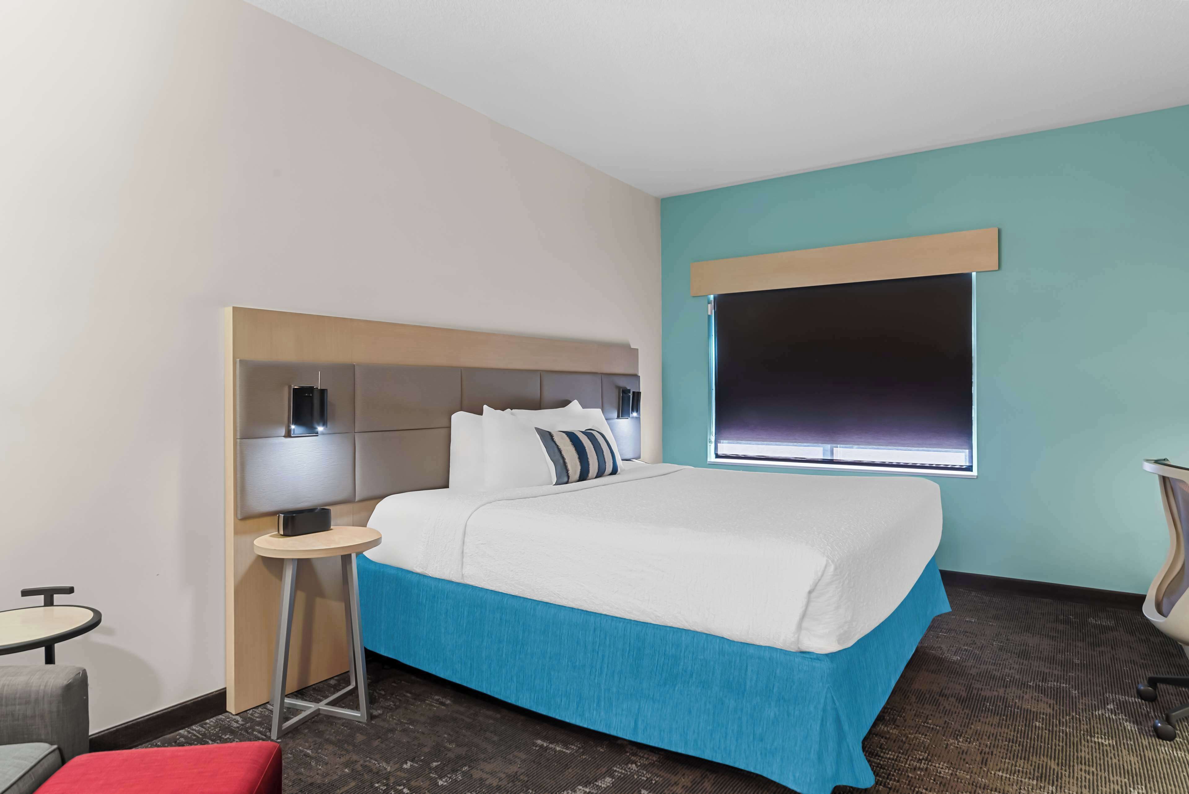 A hotel room with a bed, a small table, a chair, and a window.