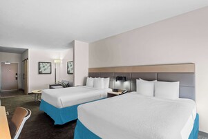 Una habitación de hotel con dos camas, un escritorio, una silla, una lámpara y una puerta.