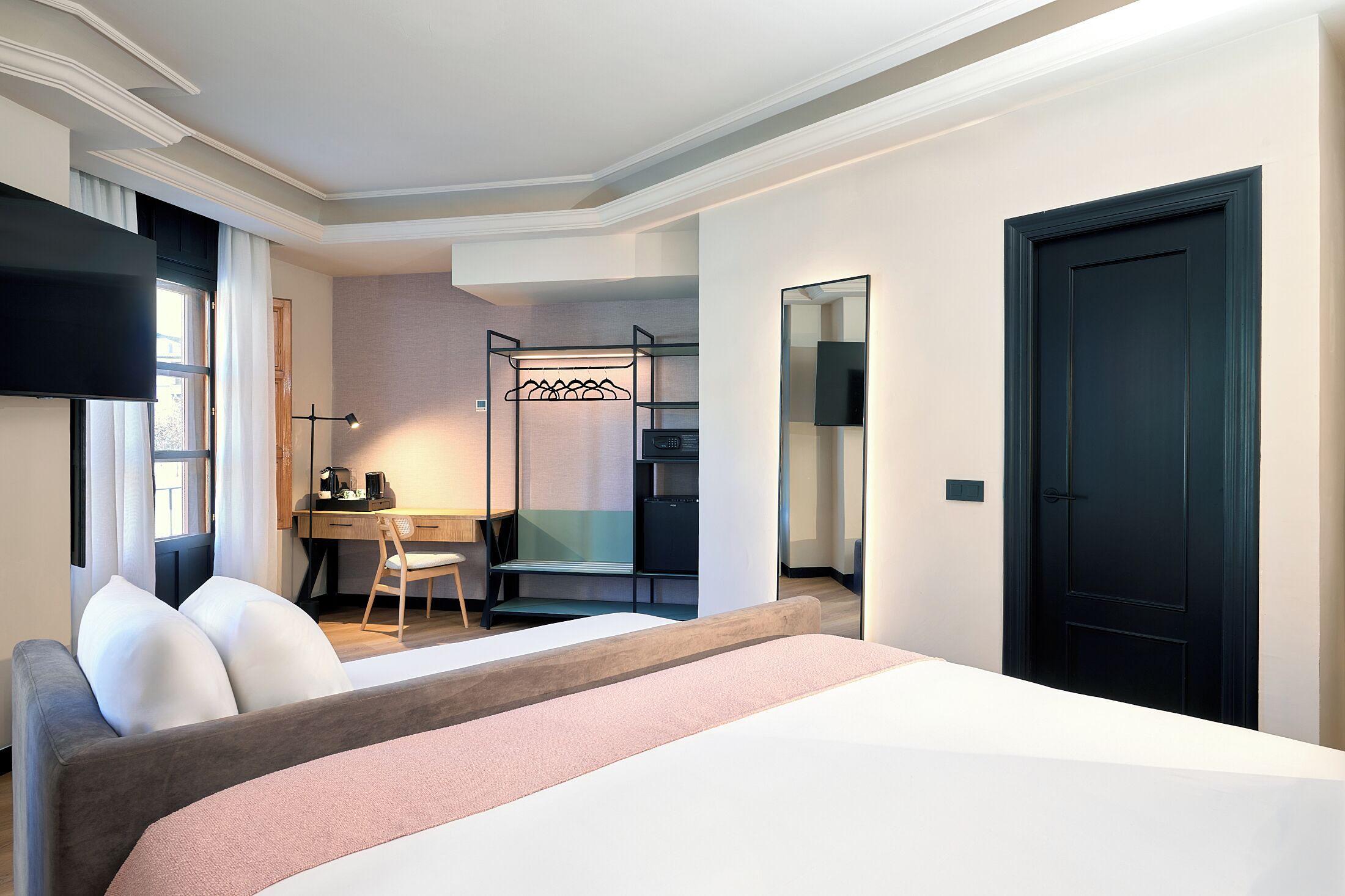 A hotel room with a bed, a desk, a chair, a TV, a wardrobe, and a door.