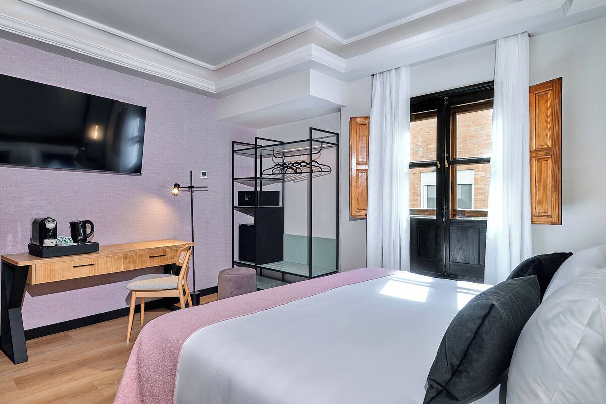 Habitación de hotel con cama, escritorio y silla, televisor, armario y ventana con cortinas.