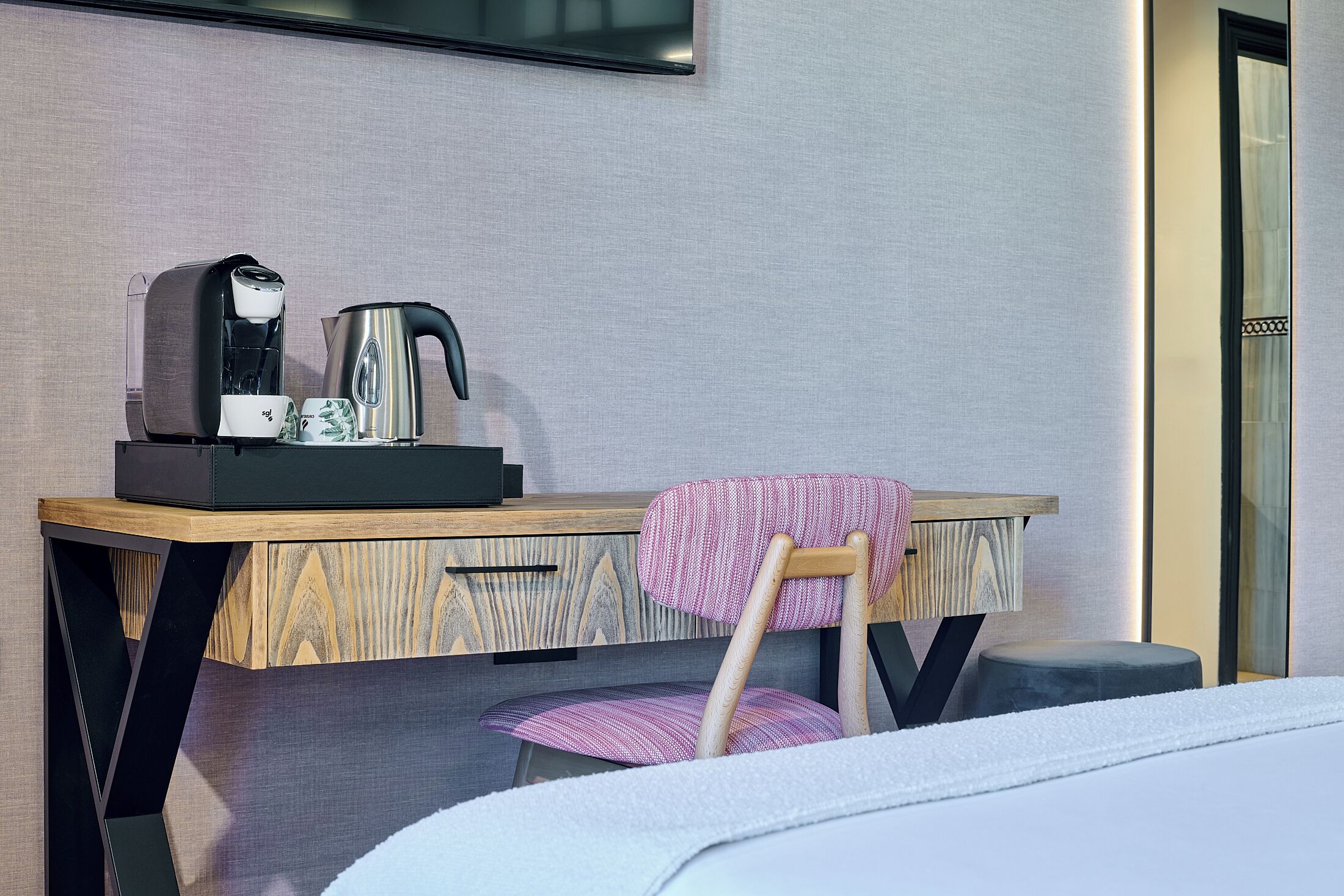 Habitación de hotel con un escritorio de madera, una silla, una cama y un televisor montado en la pared.