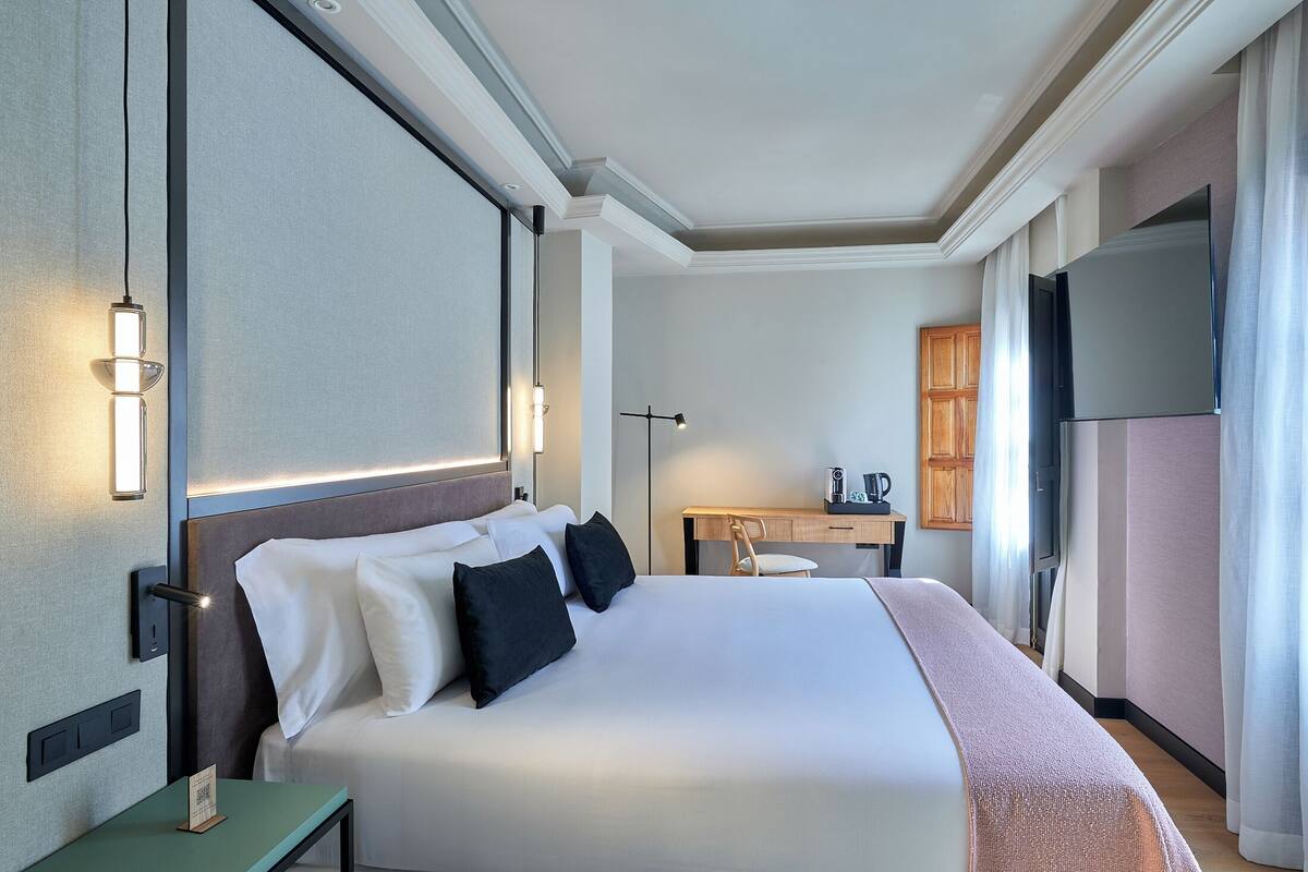 Habitación de hotel con una cama grande, mesitas de noche, un escritorio, una silla, un televisor de pantalla plana y una lámpara en el techo.