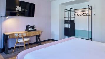 Habitación de hotel con cama, escritorio con silla, televisión, cafetera y perchero.