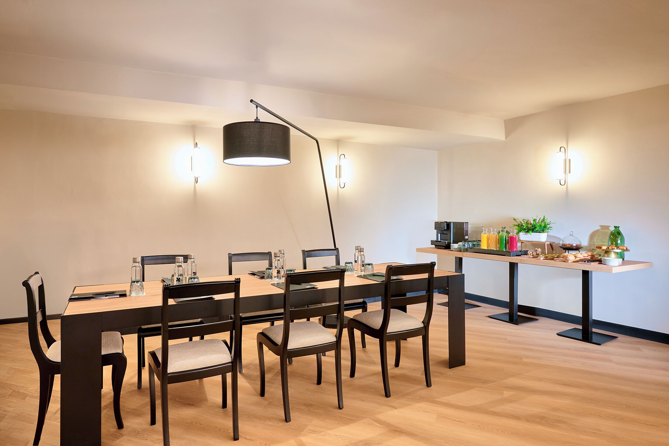 Ein moderner Essbereich mit einem langen Tisch, dunklen Stühlen, einer schwarzen Stehlampe und Wandleuchten.