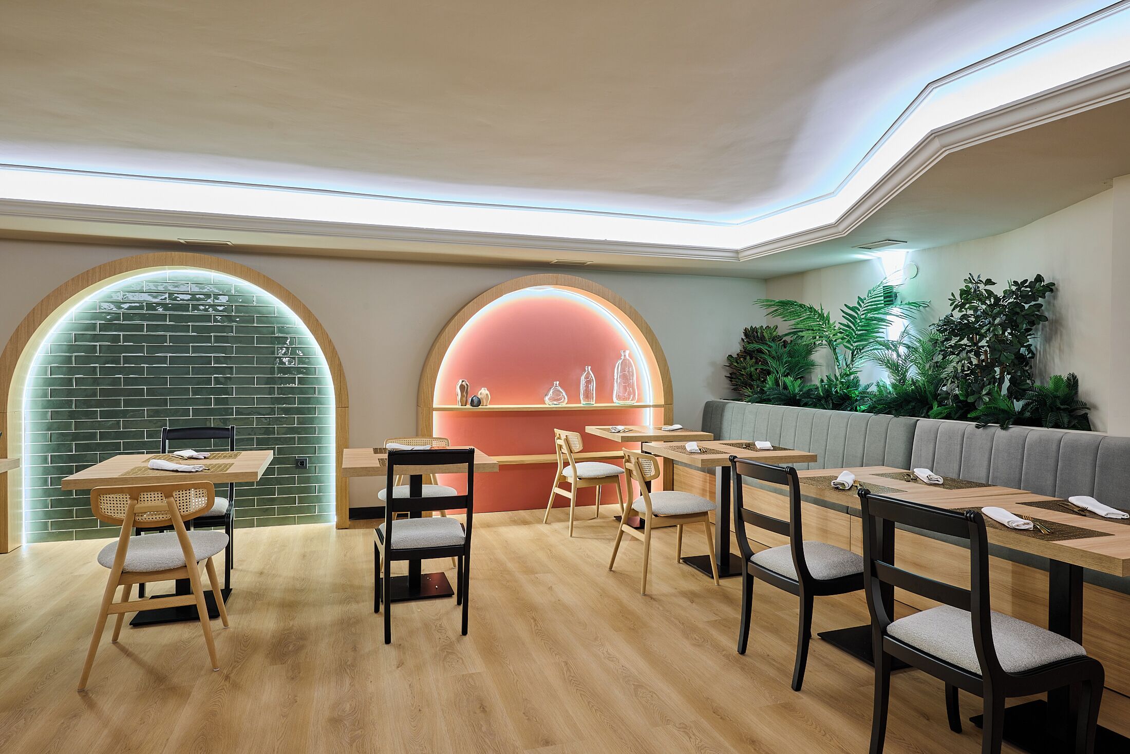 A modern dining area with wooden tables and chairs, a brick wall with a neon sign, and a green wall with plants.