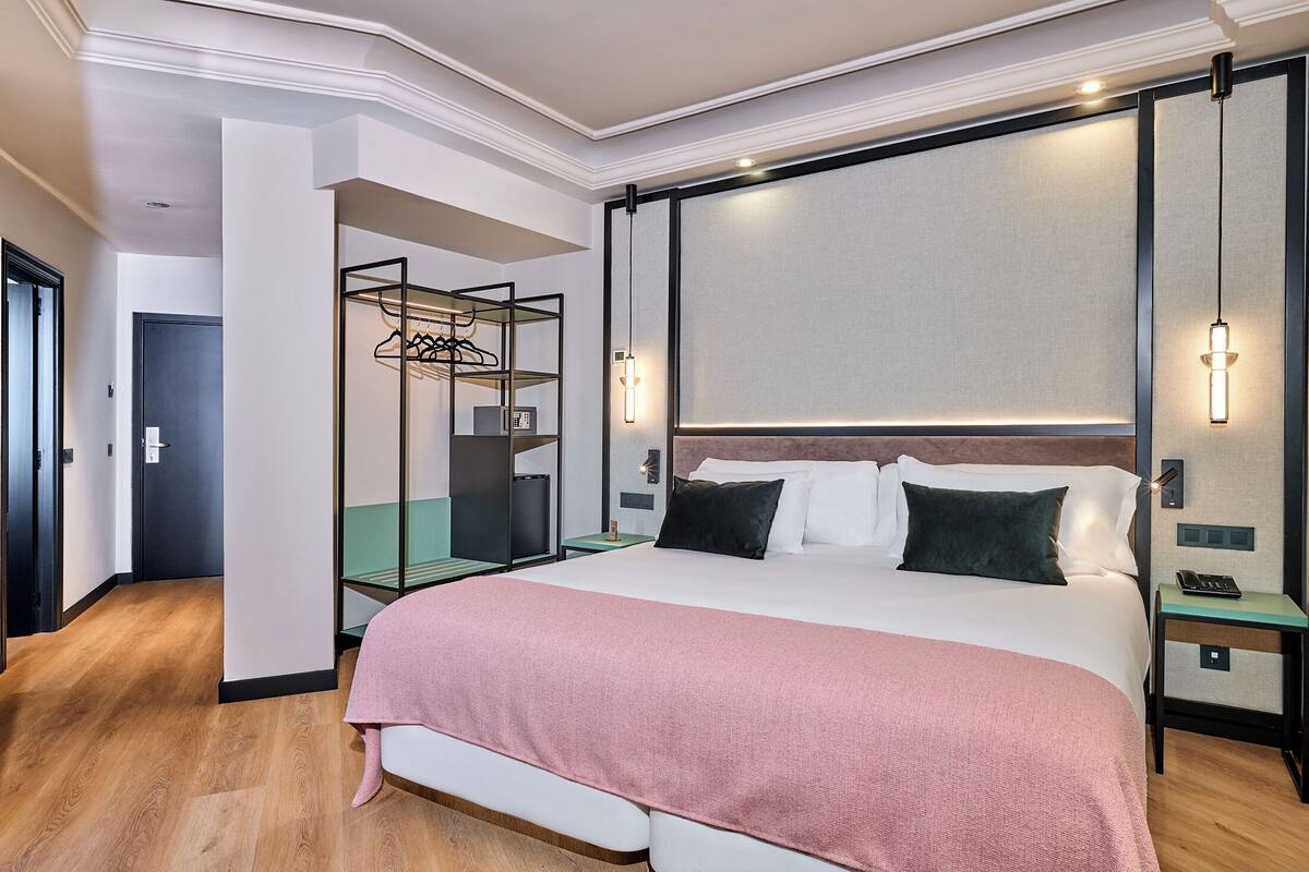 Habitación de hotel con una cama grande, una mesita de noche, un armario y una lámpara colgante.