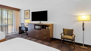 A hotel room with a bed, a desk with a chair, a television, a lamp, and a window with curtains.