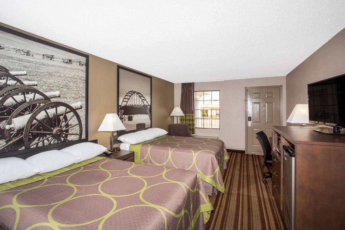 Une chambre d’hôtel avec deux lits, un bureau, une chaise, une télévision et une fenêtre avec des rideaux.