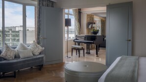 A spacious living room with a grand piano, a sofa with decorative pillows, and a large window offering a city view.
