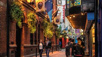 A cobblestone street with brick buildings, a clock tower, and hanging flags.