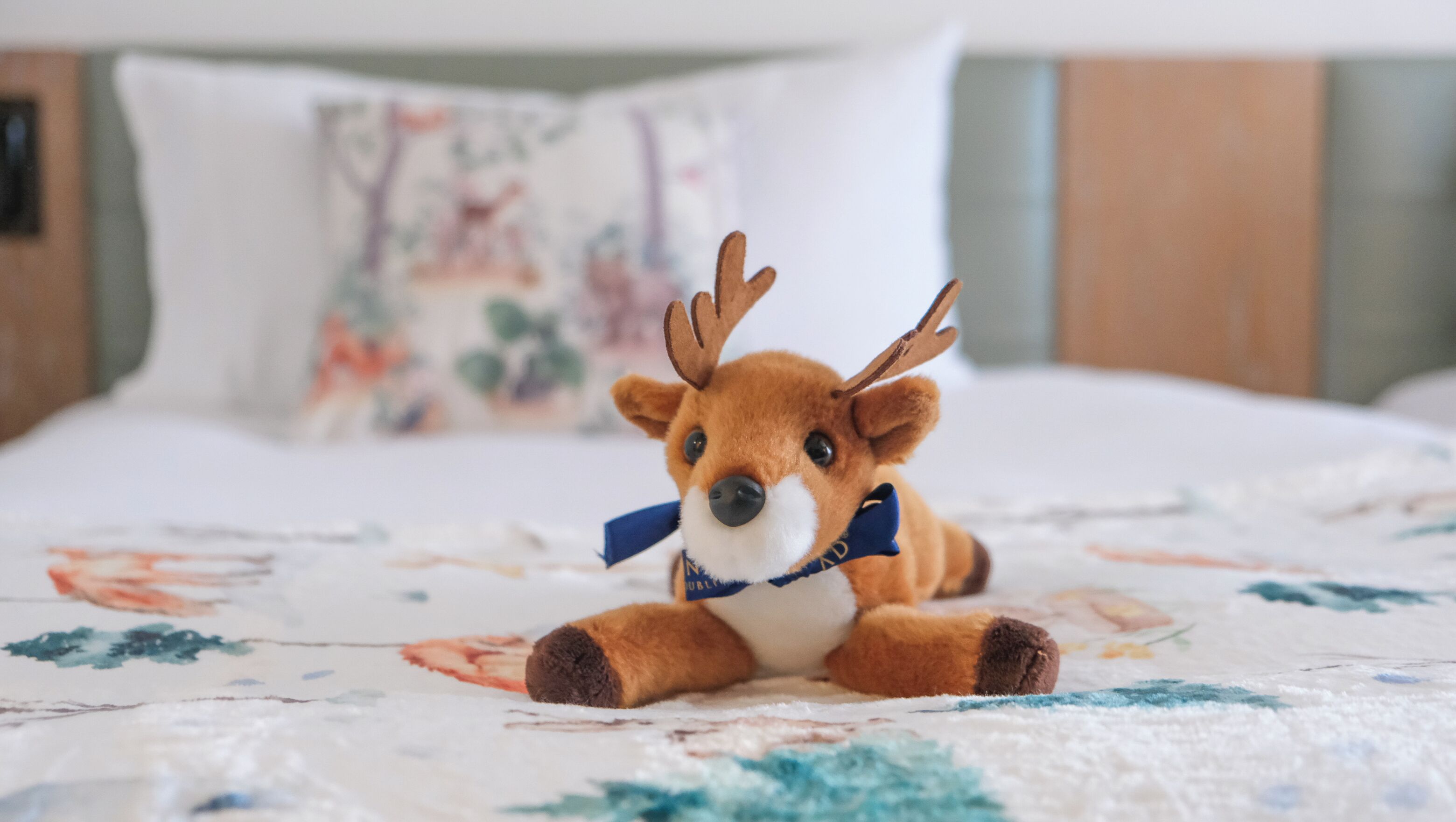 A plush toy reindeer on a bed with a floral-patterned bedspread.