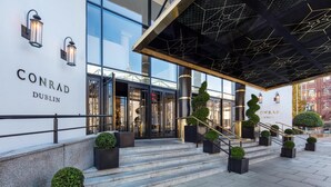 A modern hotel entrance with glass doors, a staircase, and outdoor seating.