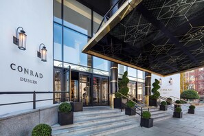 A modern hotel entrance with glass doors, a staircase, and outdoor seating.