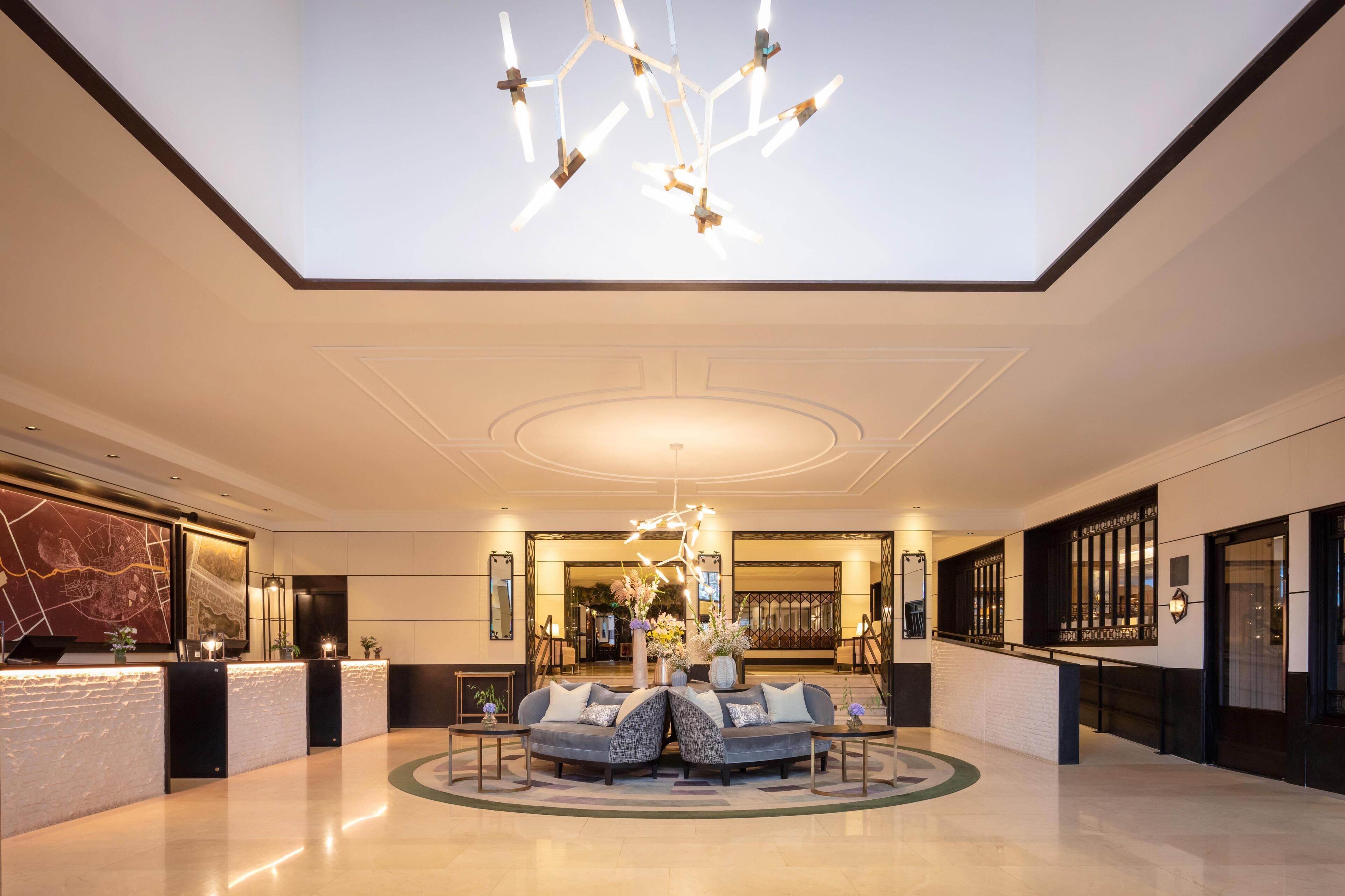 En rummelig lobby med et centralt siddeområde, en receptionsdisk og en moderne lysekrone.