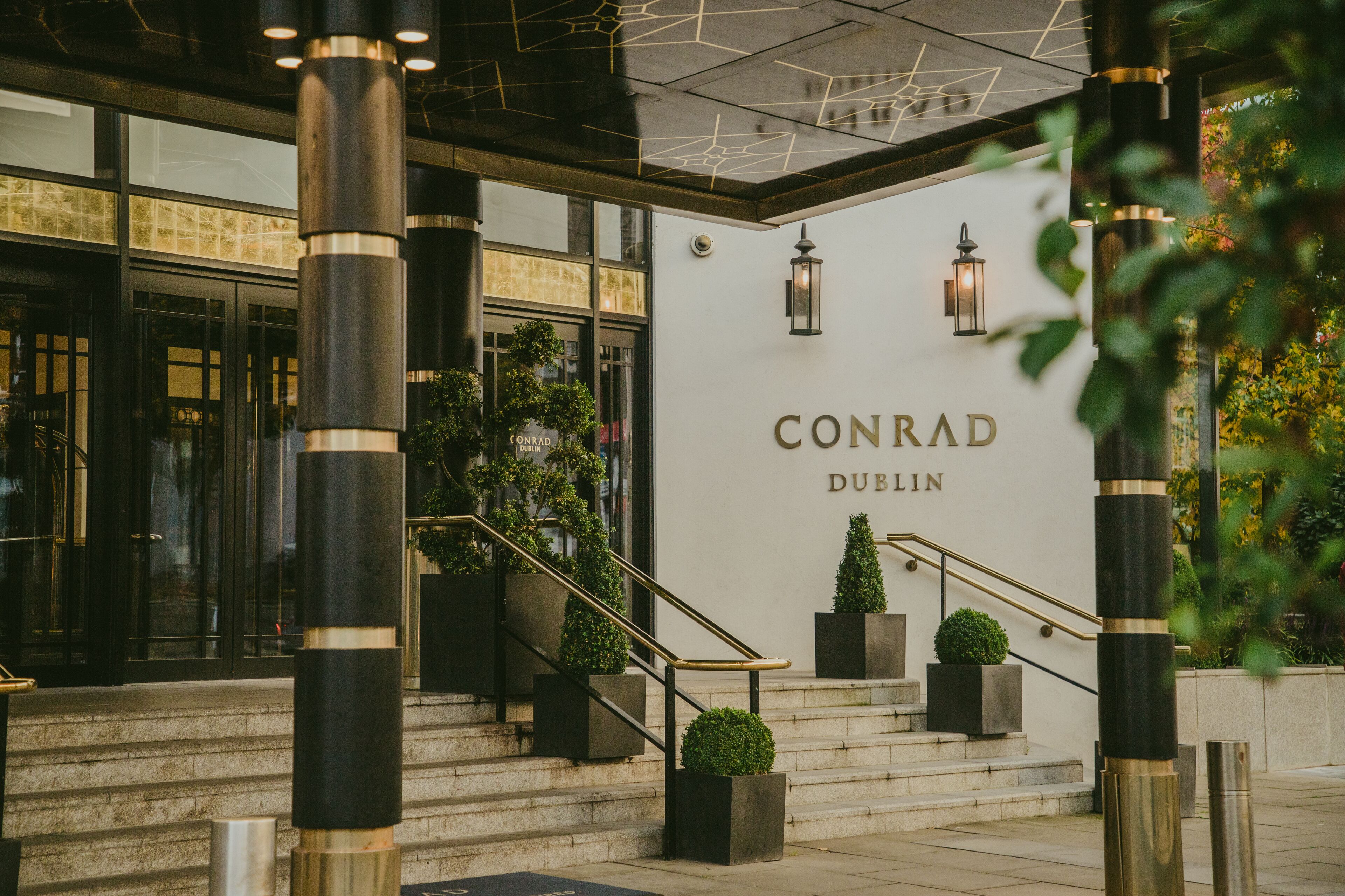 A hotel entrance with a staircase, black bollards, and a sign reading "CONRAD DUBLIN".