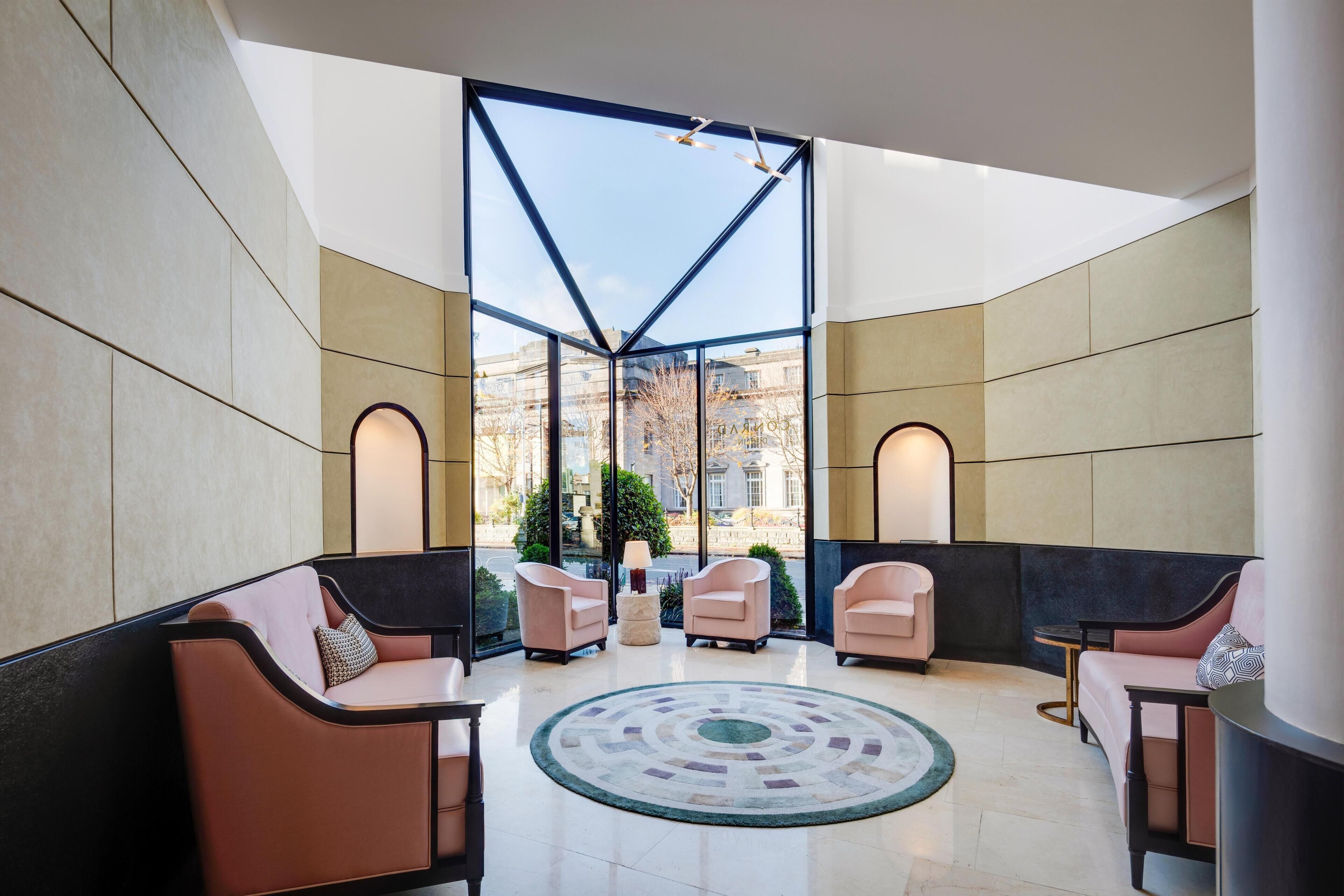 Un hall d’entrée moderne, doté d’espaces aménagés avec des sièges, d’un grand tapis central et de grandes fenêtres offrant une vue sur la ville.