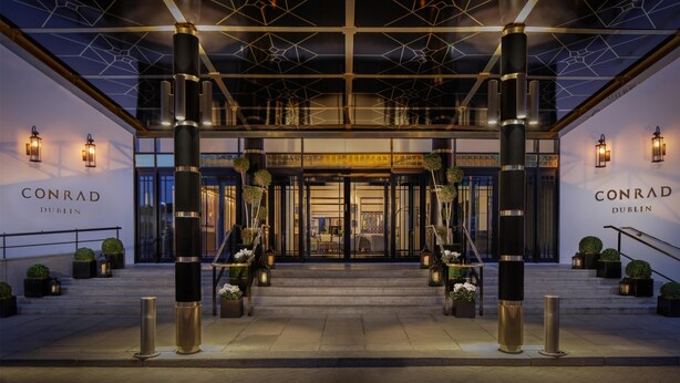 The entrance of Conrad Dublin hotel with a modern design, featuring large pillars, a geometric ceiling, and a welcoming staircase. - Conrad Dublin (Dublin)
